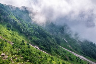 Yüksek dağların yeşil yamaçları bulutların ve sisin içinde gizlidir. Bulutlu bir günde dağlarda yoğun sis var. Yazın yüksek dağlarda eriyen karlar.