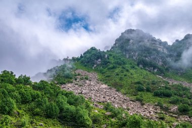 Bulutlu bir günde taşlı yeşil dağ yamacı. Kalın bulutlu dağ manzarası.