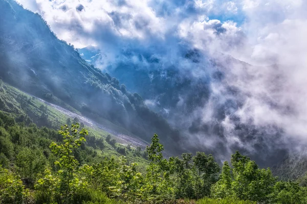 山の峡谷で重い霧と雲 曇りの夏や春の日に山の中で緑の植生 高い山の中で夏に融ける雪の層 — ストック写真