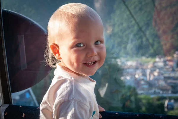 一个一岁大的小男孩坐着绿色背景的漏斗旅行的肖像 可爱的小男孩喜欢在暑假乘坐缆车 和孩子们一起旅行 — 图库照片