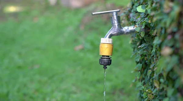 Água da torneira exterior gotejamento, fundo verde ou jardim . — Fotografia de Stock