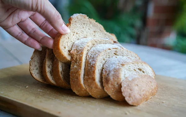 Mão segurando fatias de pão sourdough na tábua de madeira — Fotografia de Stock