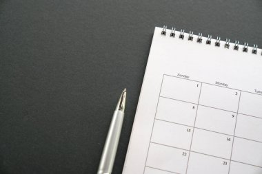 Koyu arkaplanda beyaz takvim, fotokopi alanı, yanında kalem. İş toplantısı programı, proje dönüm noktası veya seyahat planı veya hatırlatıcı kavram.