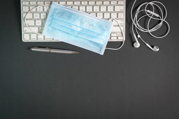 Coronavirus salgını sırasında evdeki ofis masasının üst görüntüsü. Klavye, kalem, yüz maskesi ve kulaklıkla. Uzayı kopyala Uzaktan çalışmak ya da ev kavramından çalışmak.