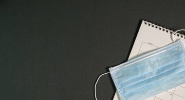 Takvim ve cerrahi maske ile siyah renkli ofis masasının üst görüntüsü. Boşluğu kopyala.