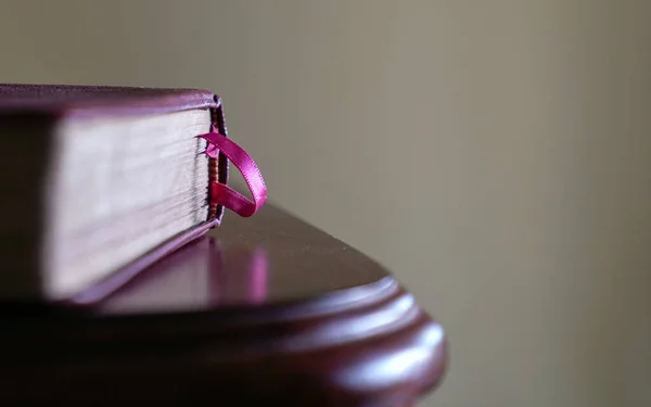 Book with pink book mark on the side of wood table. Space for text.