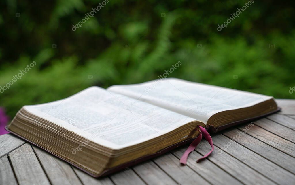 Open bible on wooden table. Soft blur effect with focus on book mark. Green nature at background.