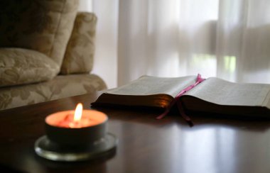 Masanın üzerinde yanan bir mumla İncil 'i aç. Konforlu ev ortamı.