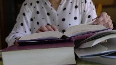 Masadaki diğer kitaplarla açık bir kitabın sayfalarını çeviren kadın. Eğitim ya da araştırma kavramı.