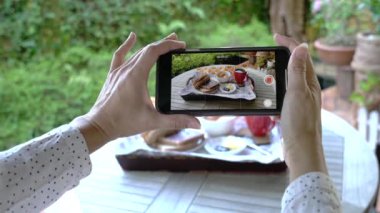 Kadın kahvaltısını cep telefonuyla videoya çekiyor. Sosyal medya kavramı.