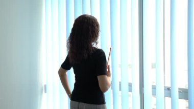 İş kadınının elinde bir dosya, ofis pencerelerinin yanında durup dışarıya baktığı arka plan görüntüsü..