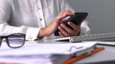 İş kadını ofis masasında cep telefonuyla mesaj atıyor. Yakın görünüm.
