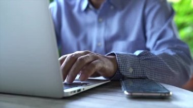 İş adamı evde bilgisayarını ve cep telefonunu tamir ediyor. Bahçe arkaplanı.