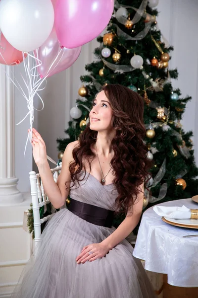Bella giovane donna in abito da sera di lusso con palloncini d'aria su sfondo di Natale — Foto Stock