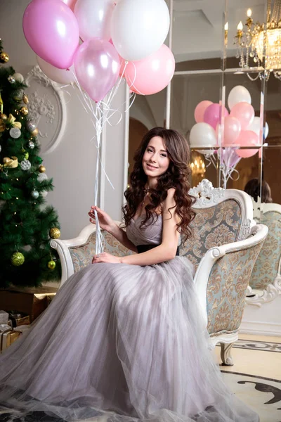 Mooie jonge vrouw in luxe avondjurk met lucht ballonnen over Kerstmis achtergrond — Stockfoto