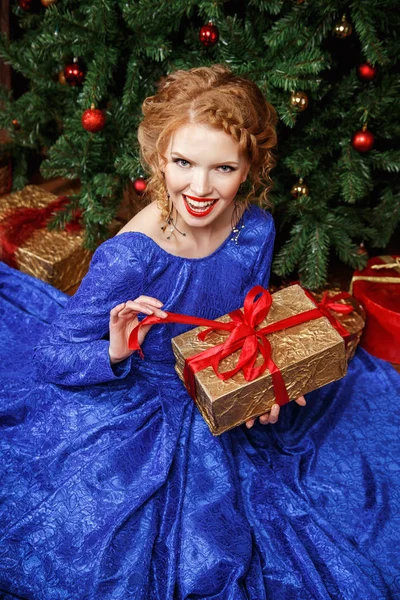 Pretty cheerful young lady in a blue evening dress over christmas background — Stock Photo, Image