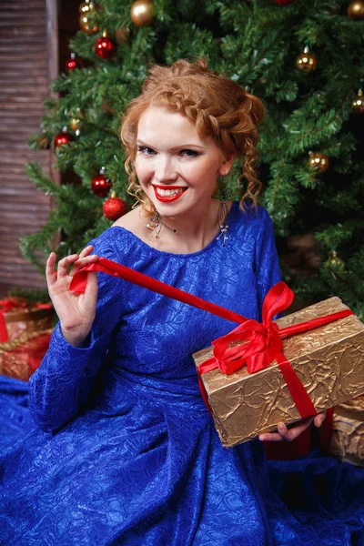 Pretty cheerful young lady in a blue evening dress over christmas background — Stock Photo, Image