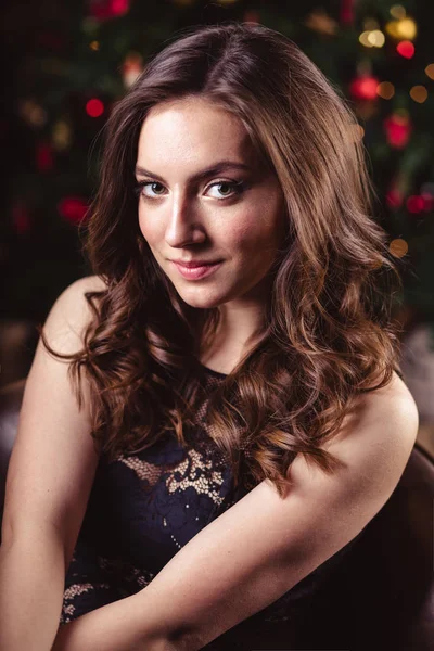 Portrait of young brunette woman in a black dress over christmas background — Stock Photo, Image