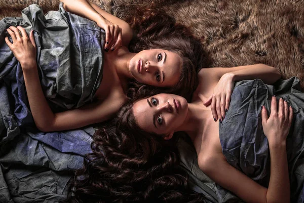 Beautiful twins young women with natural make-up and hair style lying with their curly hair surround them — Stock Photo, Image