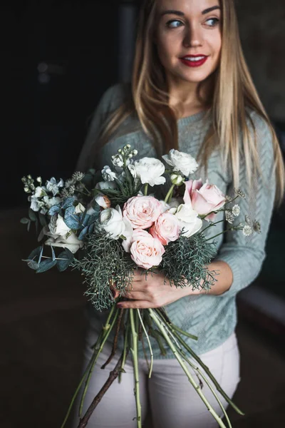 Florist at work: pretty young blond woman holds fashion modern bouquet of different flowers