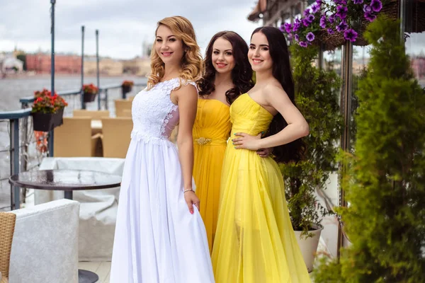 Noiva bonita e duas damas de honra em vestidos semelhantes amarelos em conjunto em um terraço de verão um restaurante do mar — Fotografia de Stock