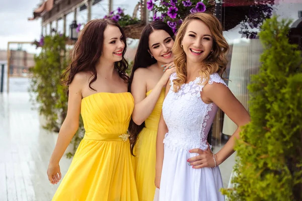 Noiva bonita e duas damas de honra em vestidos semelhantes amarelos em conjunto em um terraço de verão um restaurante do mar — Fotografia de Stock