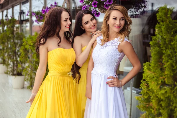 Жених и две невесты в желтых похожих платьях вместе на летней террасе морского ресторана — стоковое фото
