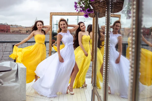 Bella sposa e due damigelle d'onore in abiti gialli simili insieme su una terrazza estiva un ristorante sul mare — Foto Stock