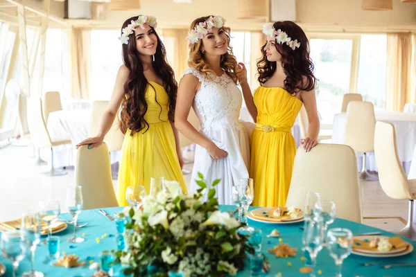 Noiva bonita e duas damas de honra em vestidos semelhantes amarelos juntos em um restaurante do mar — Fotografia de Stock