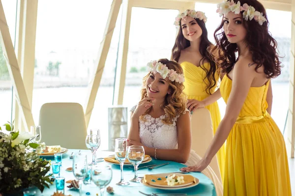 Noiva bonita e duas damas de honra em vestidos semelhantes amarelos juntos em um restaurante do mar — Fotografia de Stock