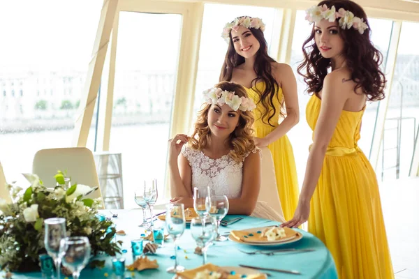 Schöne Braut und zwei Brautjungfern in gelben ähnlichen Kleidern zusammen in einem Meeres-Restaurant — Stockfoto