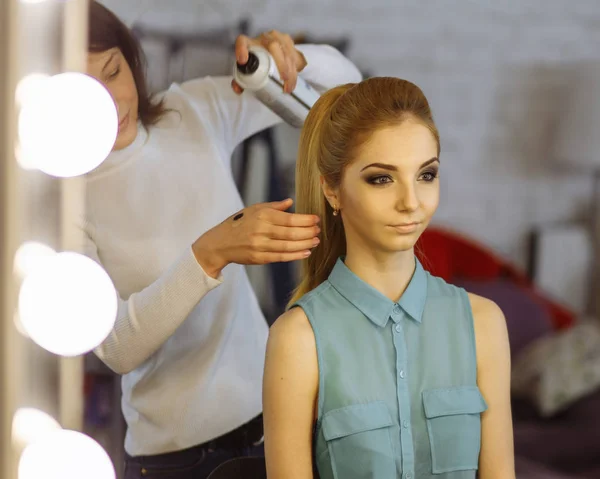 Make-up artist preparing model in a dressing room before photosession