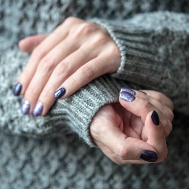 Güzel manikür, mor ve gümüş tırnak cilası, closeup fotoğraf. Arka plan gri örgü giysileri ile üzerinde eller