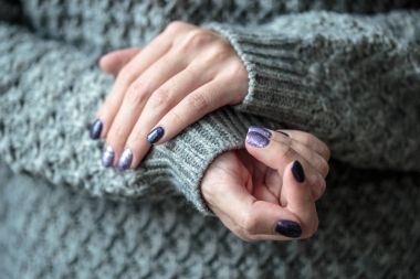 Güzel manikür, mor ve gümüş tırnak cilası, closeup fotoğraf. Arka plan gri örgü giysileri ile üzerinde eller