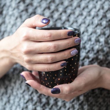 Güzel manikür, mor ve gümüş tırnak cilası, closeup fotoğraf. Arka plan gri örgü giysileri ile üzerinde eller