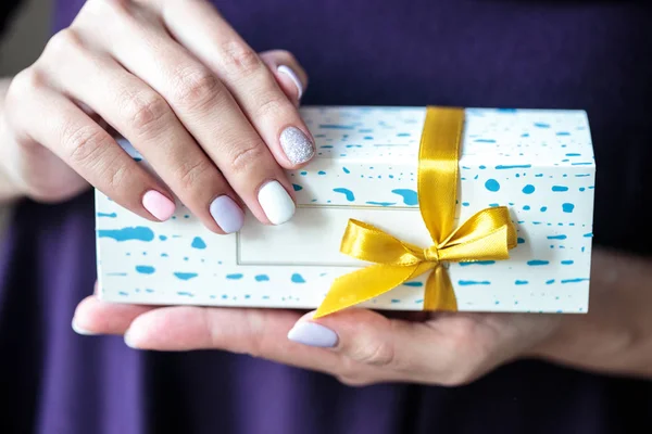 Present box with a gold bow with macaroons inside. Woman holds a box with biscuits.