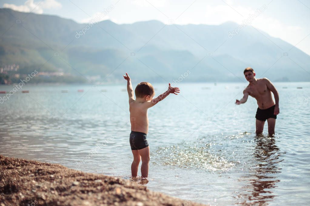 Young father and his little son play together in a water. Scenic sea and mountain view, summer time vacation