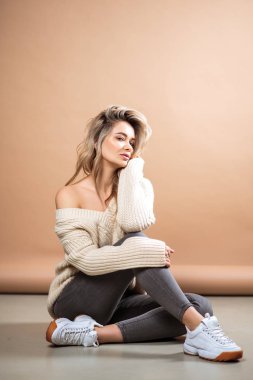 Kahverengi arka planda örülü süveter giyen güzel sarışın kadın. Sıradan tarz, moda güzellik portresi.