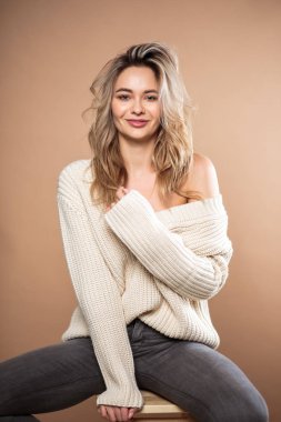 Kahverengi arka planda örülü süveter giyen güzel sarışın kadın. Sıradan tarz, moda güzellik portresi.
