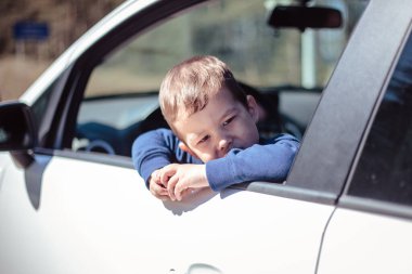 Küçük çocuk arabanın camından dışarı bakıyor.