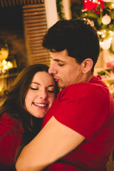 Ζευγάρι γιορτάζει μαζί Χριστούγεννα. Ελκυστική γυναίκα και όμορφος άντρας με κλειστά μάτια αγκαλιάζει κάτω από το τζάκι με κεριά, φώτα, δώρα και διακοσμημένο δέντρο. Καλή Χρονιά.. — Φωτογραφία Αρχείου
