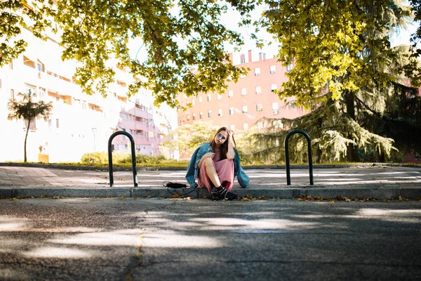 Sad young woman with sunglasses sitting on the sidewalk worried and waiting for someone in the park. Human emotion face expression,feeling, reaction body language. Emotional concept.