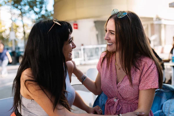 Dos chicas felices hablando en la terraza de un bar. Amigos disfrutando juntos teniendo una buena conversación sentados en una terraza cafetería. Bonitas novias riendo mientras están sentadas en un bar al aire libre . — Foto de Stock