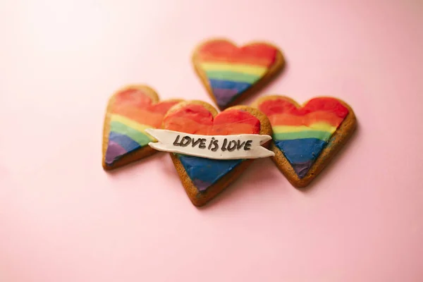 Love is love LGTB hearts cookies on a pink background. Rainbow heart cookie. Heart lgbt+ sign rainbow color stripe. Symbolic free love concept.