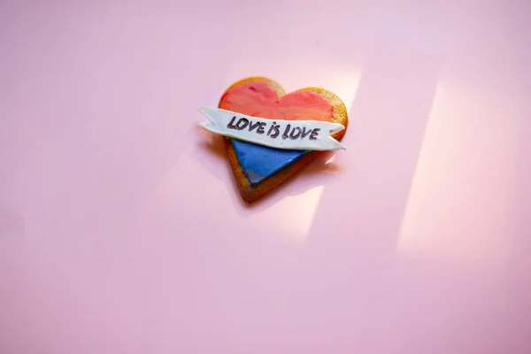 Amor es amor LGTB galleta del corazón sobre un fondo rosa. Galleta de corazón arco iris. Corazón lgbt + signo de rayas de color arco iris. Concepto simbólico de amor libre . — Foto de Stock