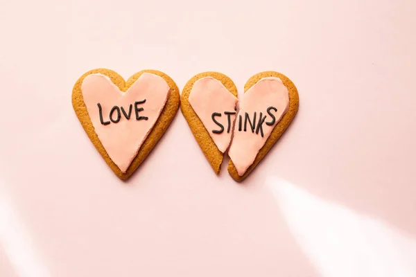 Dos galletas de jengibre corazón roto decoradas con fondant rosa con el mensaje de amor apesta. concepto de angustia . — Foto de Stock