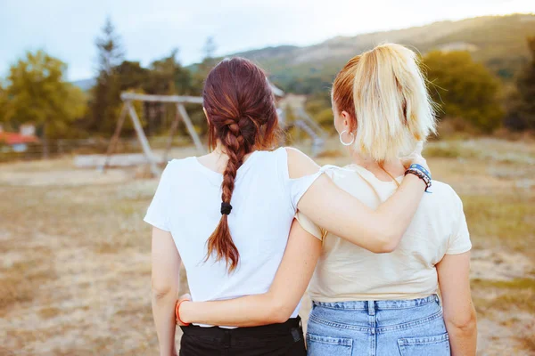 Dos jóvenes amigas en la espalda con el pelo en una trenza y el pelo rubio abrazándose en el campo. Concepto de amistad . — Foto de Stock