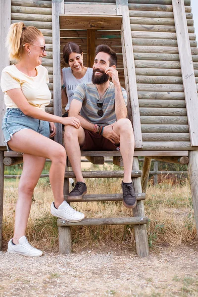 Turistler dinleniyor. Ahşap kamp merdivenlerinde oturmuş, kırsalda eğlenen ve gülen üç arkadaş grubu. Kamp macerası ve seyahat konsepti. — Stok fotoğraf