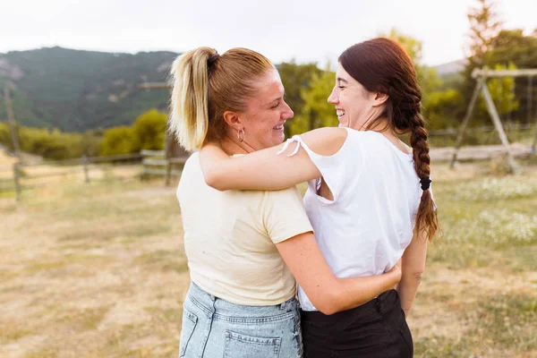 Vista trasera de novias sonriendo y abrazándose en el campo. Mejor amigo, amor y concepto de amistad . — Foto de Stock