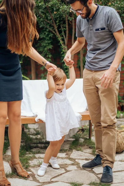 Niña rubia jugando y sosteniendo la mano de sus padres jóvenes en el jardín. Niño disfrutando con mon y papá. Amor y concepto familiar . —  Fotos de Stock